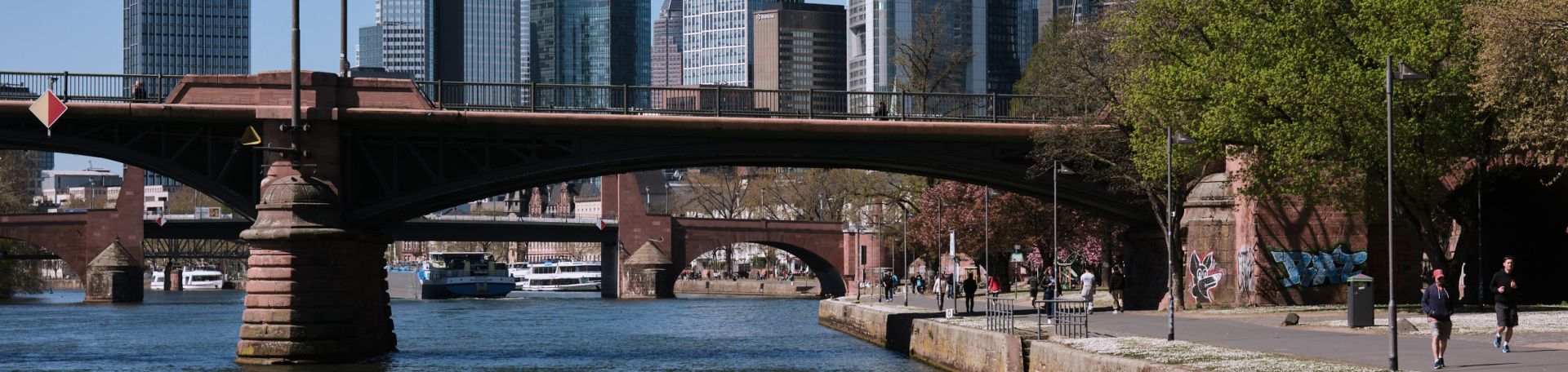 You can see the River Main. A bridge crosses the river. In the background, you can see the skyline. It is spring.