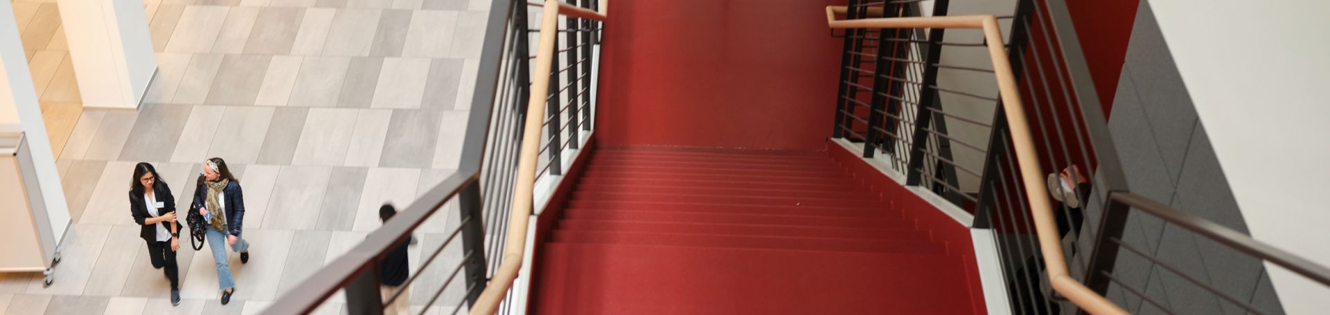 Es ist ein Teil einer Treppe im Inneren der FS Mall zu sehen. Weiter unten sind zwei Personen zu sehen, die durch die Mall gehen.